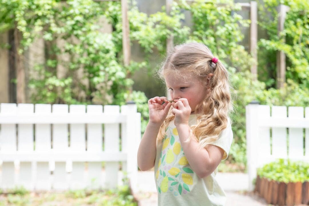 Little girl sniffs a leaf in the sensory garden at the museum.